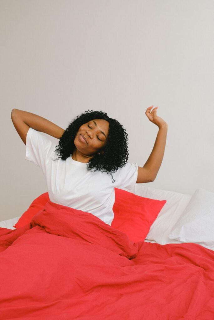 Happy African American female with eyes closed stretching in soft bed on white background